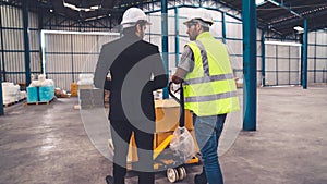 Factory workers deliver boxes package on a pushing trolley in the warehouse .