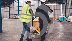 Factory workers deliver boxes package on a pushing trolley in the warehouse .