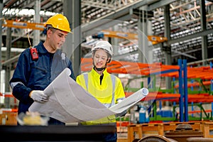 Factory workers man and woman discuss about the project using drawing paper or plan in workplace with machine and product shelves