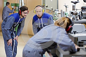 Factory workers wearing ear defenders examining machinery