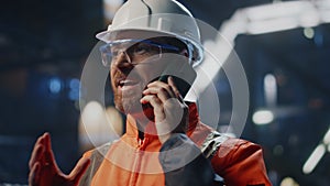 Factory workman talking mobile phone standing at industrial facility close up.