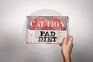 Fad Diet. Metal warning sign in a woman's hand on a white background