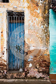 Faded blue door behind locked grate on brick wall with broken pl