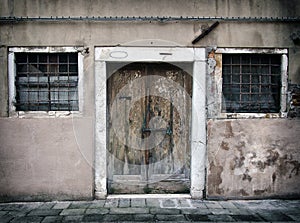 Faded old run down empty house in venice with cracked walls and bolted peeling wooden door with bars on the windows