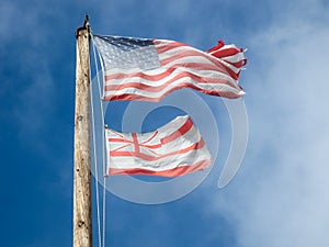 Faded and worn Hawaiian and American flags on a wooden flagpole