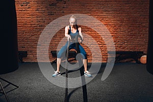 Fair-haired beautiful serious athletic woman doing battle rope exercises at gym