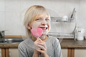 Fair-haired boy holds heart-shaped lollipop in his hands