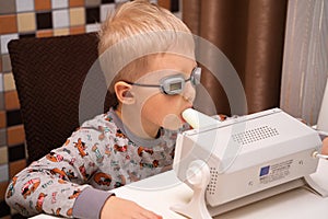 A fair-haired boy in pajamas undergoes prevention of viruses and diseases at home using a quartz germicidal irradiator. Disease