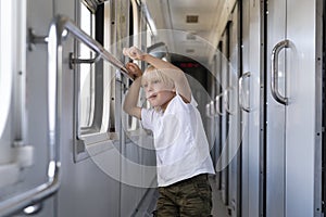 Fair-haired boy stands in railway carriage and looks out window. Rail travel