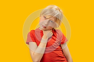 Fair-haired caucasian boy wears red T-shirt and poses for photo in studio on yellow background