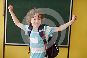 The fair-haired curly school student stand against a blackboard.