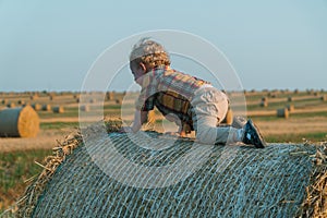 A fair-haired littleboy sits on top of a straw bale on a wheat field