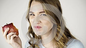 Fair haired woman biting a red apple and flirting close up