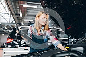 Fair-haired woman using digital tablet while diagnosing car engine.