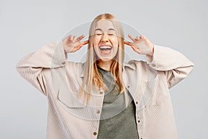 Fair-haired young woman closing her ears with hands, having happy expression, smiling broadly, anticipating to hearing the good