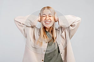 Fair-haired young woman closing her ears with hands, having happy expression, smiling broadly, anticipating to hearing the good