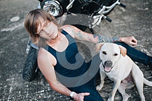 Fair man is sitting on the ground at his motorbike with a dog