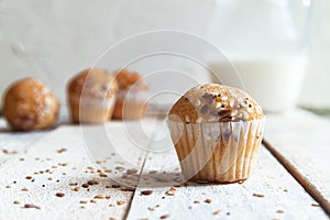 Fairy cakes baked with some sessame seeds on a white wooden table against a white background in a rustic kitchen. Jar of milk