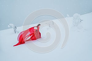 Fairy tale girl on polar winter landscape. Young beautiful woman in long red dress over winter hill background and snowfall