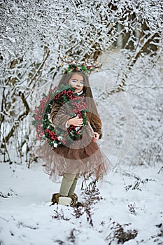 Fairy tale girl. Portrait a little girl in a deer dress with a painted face in the winter forest. Big brown antler