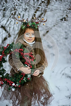Fairy tale girl. Portrait a little girl in a deer dress with a painted face in the winter forest. Big brown antler