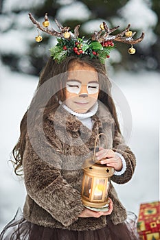 Fairy tale girl. Portrait a little girl in a deer dress with a painted face in the winter forest. Big brown antler