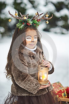 Fairy tale girl. Portrait a little girl in a deer dress with a painted face in the winter forest. Big brown antler