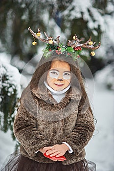 Fairy tale girl. Portrait a little girl in a deer dress with a painted face in the winter forest. Big brown antler