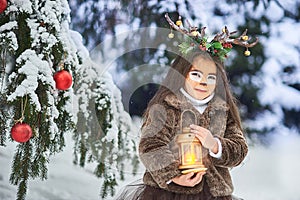 Fairy tale girl. Portrait a little girl in a deer dress with a painted face in the winter forest. Big brown antler