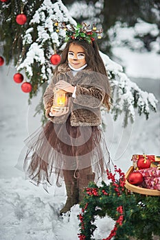 Fairy tale girl. Portrait a little girl in a deer dress with a painted face in the winter forest. Big brown antler