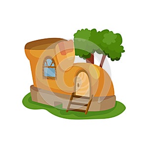 Fairy-tale house in form of yellow shoe with little window and wooden ladder in front of entrance door. Green tree on