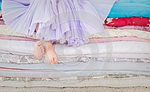 The fairy tale the princess on a pea. Little girl in lilac tatu skirt sitting on the high bed. Bare foot if the girl