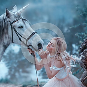 A fairy in a tender vintage dress hugs a unicorn. Fantastic magical, radiant horse. Background river and forest. Blonde