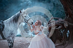 A fairy in a tender vintage dress hugs a unicorn. Fantastic magical, radiant horse. Background river and forest. Blonde photo