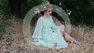 Fairytale character. Girl with wildflower crown in green dress sits in forest. Paganism. Forest spirit, mavka, fairy. 4K Resolutio