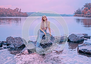 Fairytale sea queen with pink long hair, jellyfish sitting on stones, dreamily looks at purple sky, mermaid splashes