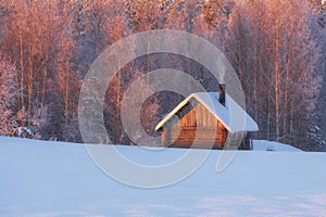 Fairytale small wooden house or sauna near the winter forest in the snow and smoke from the chimney. Winter Christmas landscape