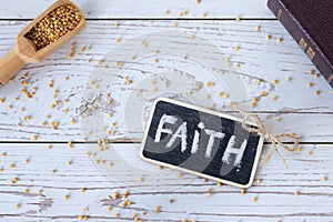 Faith handwritten text word with chalk, spoon with mustard seeds, and closed holy Bible book on wooden background