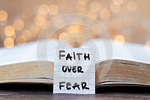 Faith over fear, handwritten quote and open holy bible book with bokeh light background
