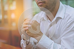 A faithful Asian young male hands in prayer gesture sitting alone on sofa at church pray and hope for good luck, success, forgiven