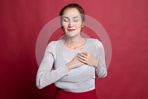 Faithful woman closes eyes and keeps hands on chest near heart, shows her kindness