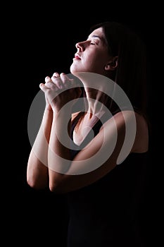 Faithful woman praying, hands folded in worship to god with head up and closed eyes