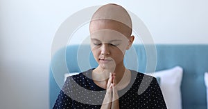Faithful young oncology center bald female patient praying indoors.