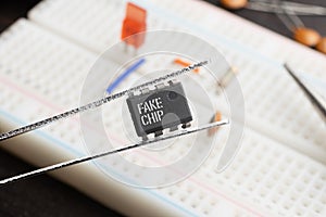 Fake chip concept: An integrated circuit held with tweezers on top of a breadboard populated with electronic components