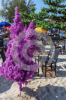 Fake christmas tree on tropical beach with chairs and tables around