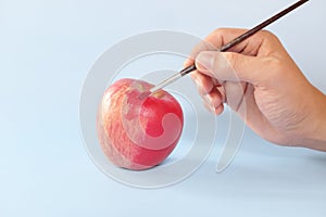 Fake food, coloring, fraud and fraudulent food concept. Hand painting an apple with artificial red colorant or paint.