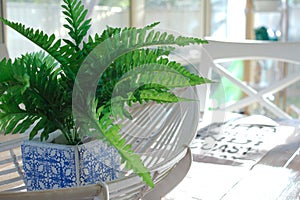 A fake green fern in a blue and white pot sits in a cane basket on a wooden dining table.