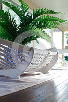 A fake green fern in a blue and white pot sits in a cane basket on a wooden dining table.