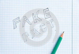 Fake news concept. Fake - Fact. Drawing in a notebook and pencil. Erased word fact. Fake information concept. Top view
