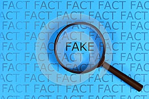 Fake News concept with words `fact` in row and single word  `fake` highlighted by magnifying glass on blue background